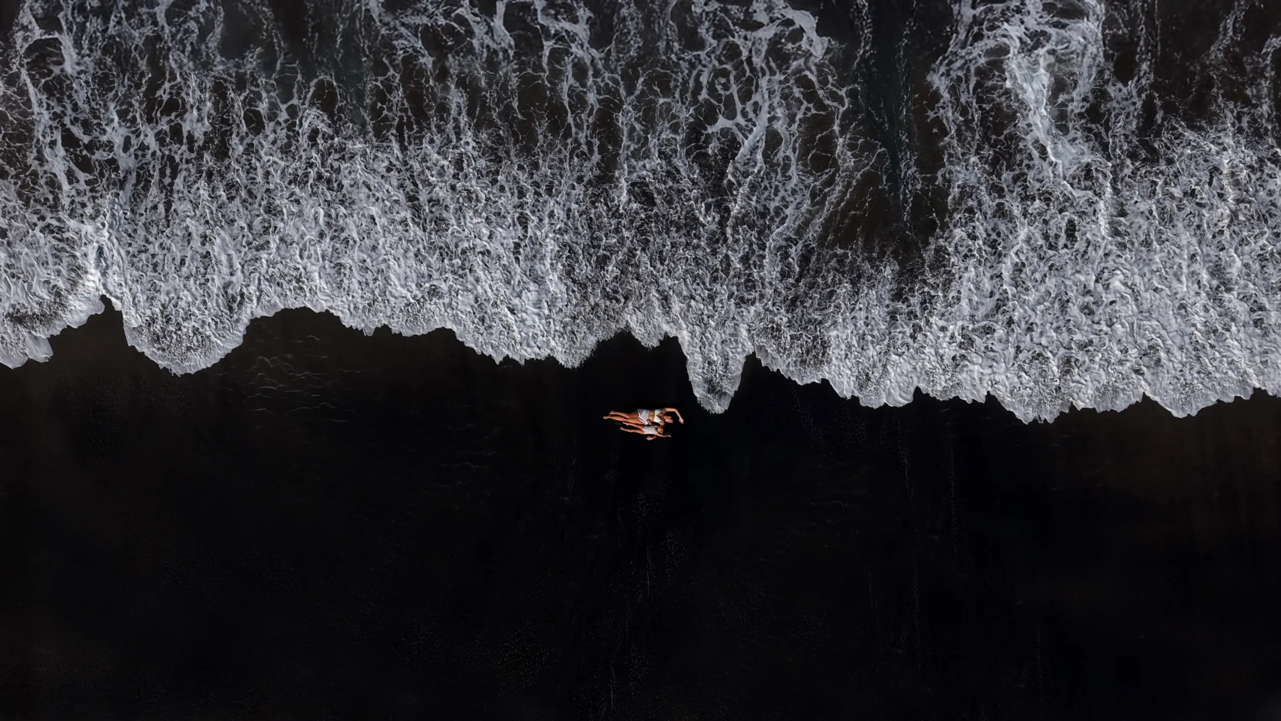 Sense of place: aerial view of black sand beach, distant swimmers
